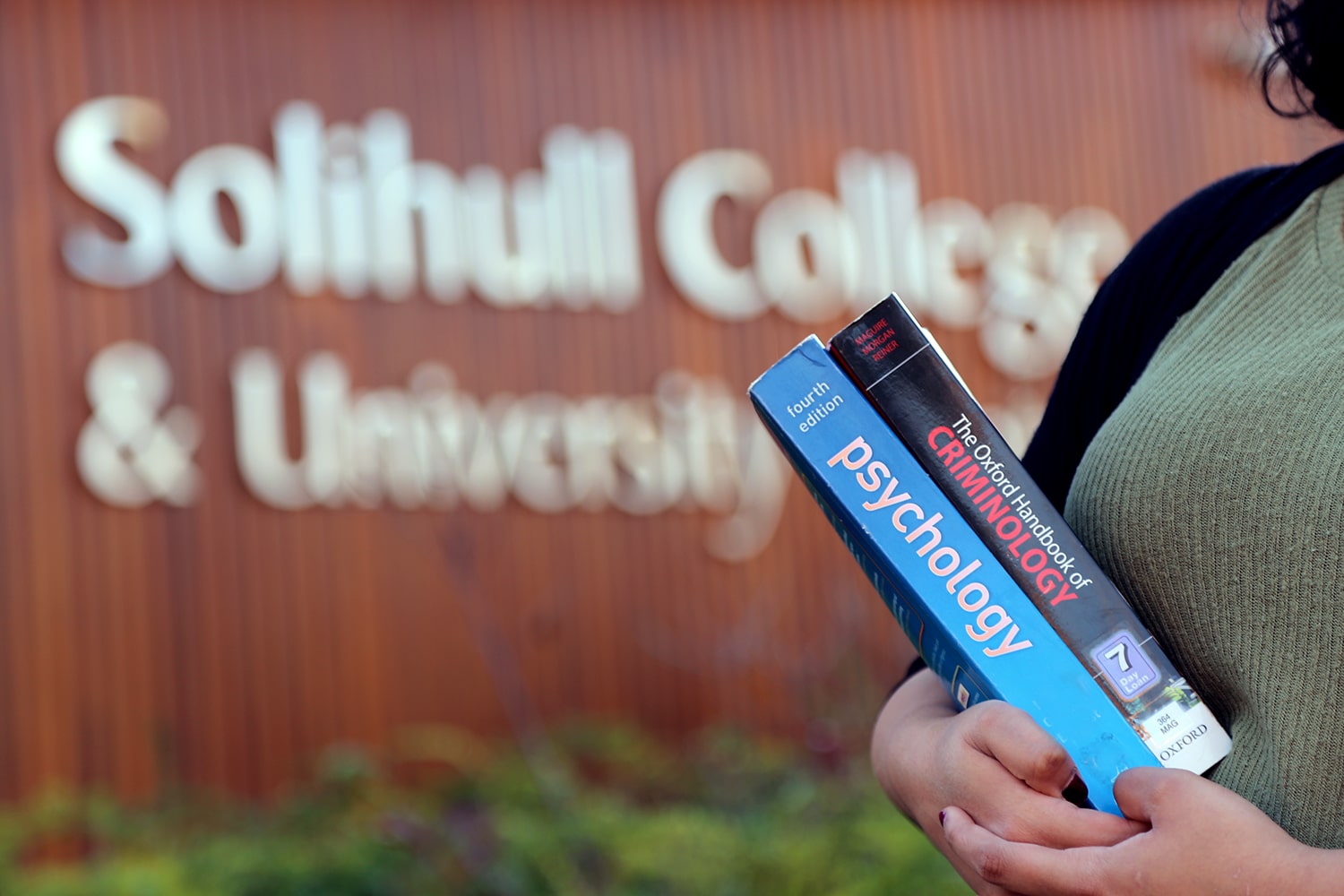 Girl stands holding books in front of college.