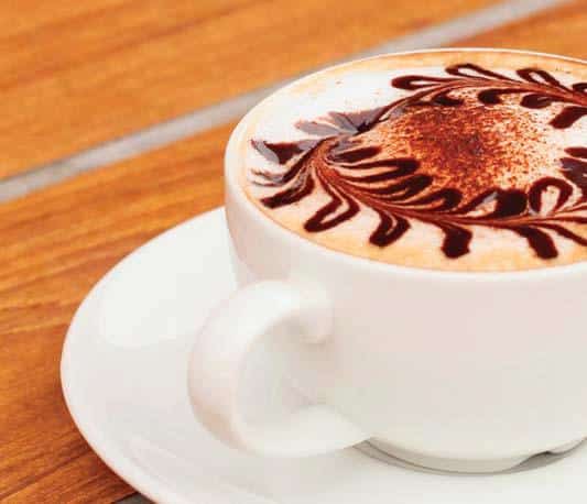Coffee in cup and saucer with decorative pattern in foam.