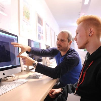 a teacher pointing at a screen with a graphic design student in front