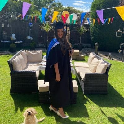 Lauren stands in her garden in a graduation gown.