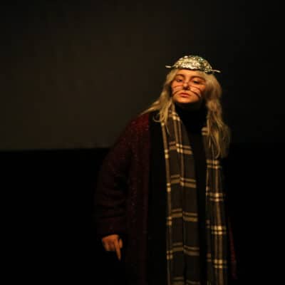 A young female performer looks out into the crowd dressed as an older woman.