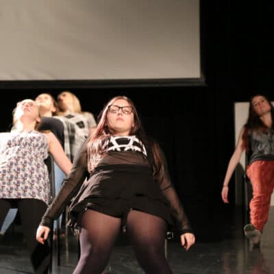 Perfoming Arts students perform sat on chairs in a big group.