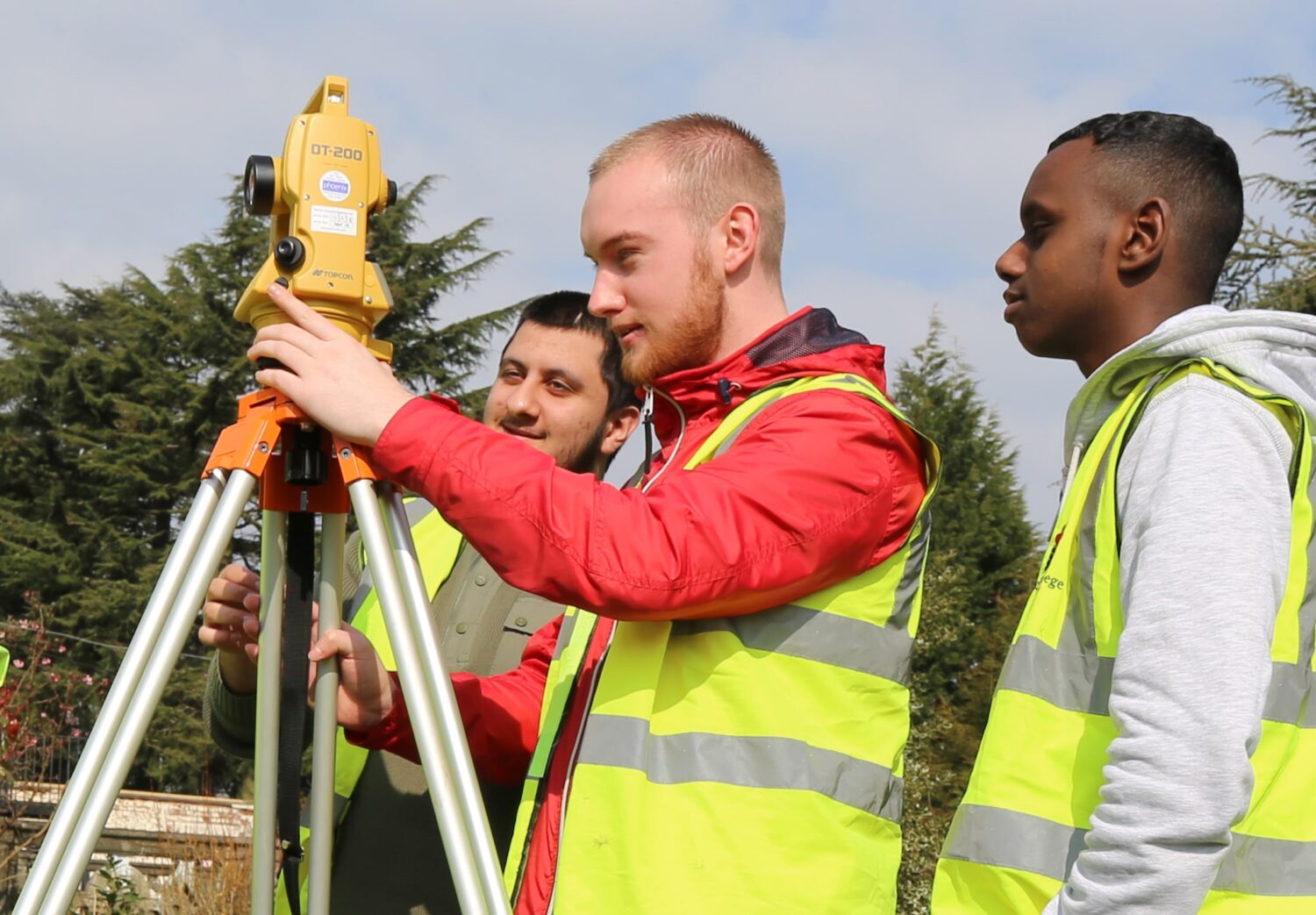 two students and a teacher measure with some surveying equipment outside on campus