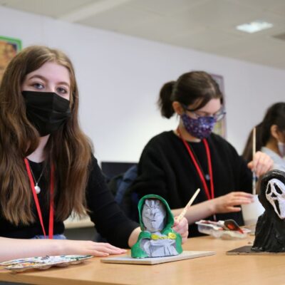 Student Jenna sat in a classroom painting her model on the desk with others sat behind her.