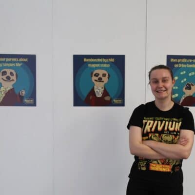 an artist stood in front of her design work portraying meerkats