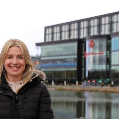 Annabelle stands in a coat in front of Resorts World next to a lake.