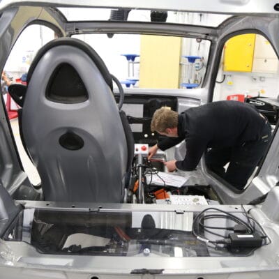 a student leans into the body of a car with a tool