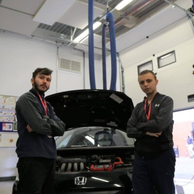 two students stand in front of a hybrid car