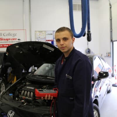 a student stands next to a car bonnet in college overalls