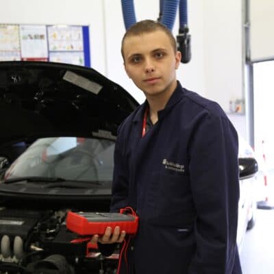 a student stands before the bonnet of a car with a mechanical piece of equipment in his hand