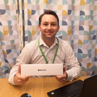 Jonathan Eastwood holding his Apple Watch in his home office