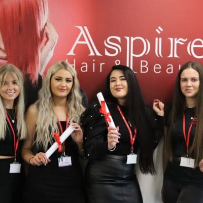 four female hair apprentices stand in the aspire studio with their scrolls after completing their apprenticeships