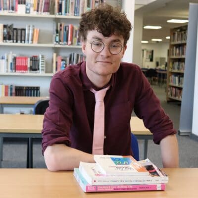 Josh Griffiths sat in the library smiling at the camera at solihull college