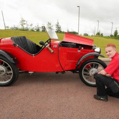 Tianna kneels near a wheel of an old classic car