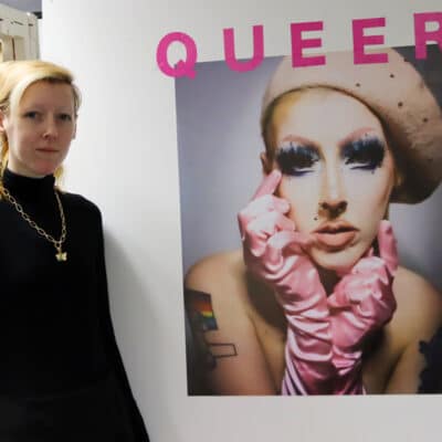 student standing in front of self portrait with 'Queer' written in pink