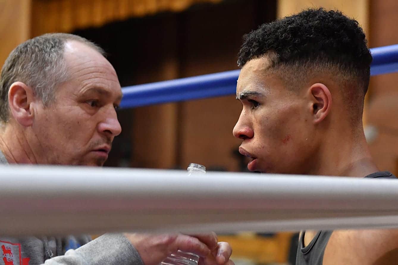 two men in corner of boxing ring zoomed into face coach is cleaning boxer's face