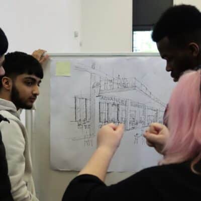 3 students looking at drawing of bulding with staff member