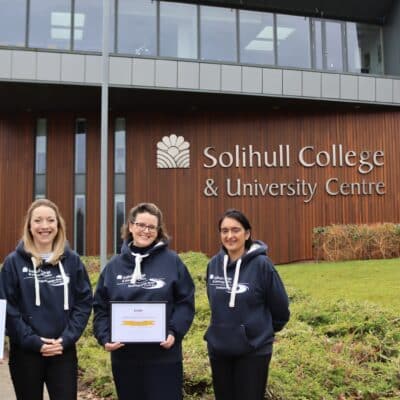 4 staff members standing in front of college building holding certificates