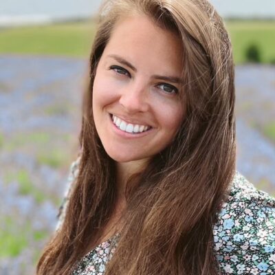 Rachel is looking at the camera smiling and has long brown hair. The background is blurred but is in a lavender field.