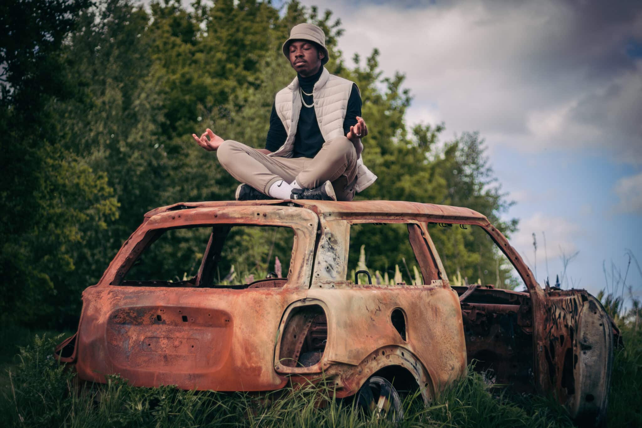 Man meditating on top of burn out car