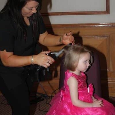 woman styling hair of child wearing pink dress