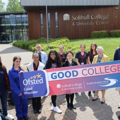Students and three staff members standing in front of College campus with Ofsted 'Good' Banner