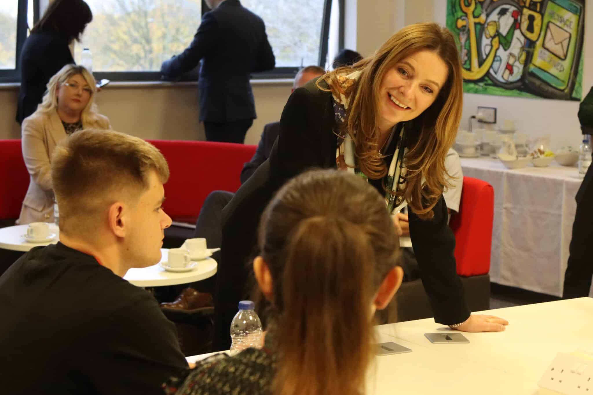 MP leans on table and talks to two students