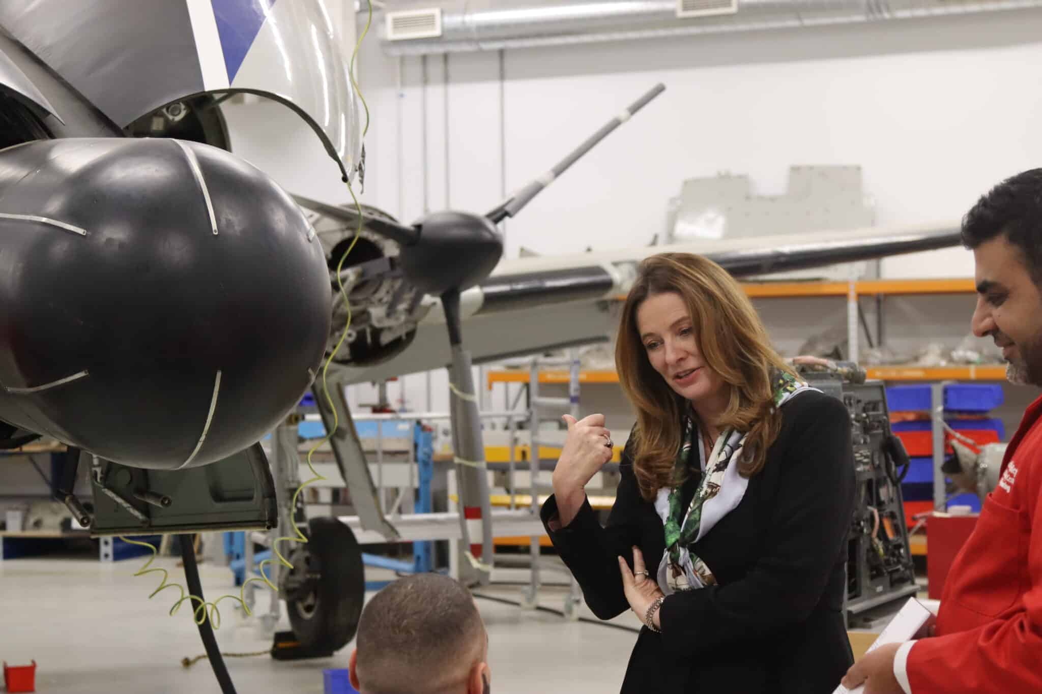Aircraft hangar in background as MP and lecturer talk to students