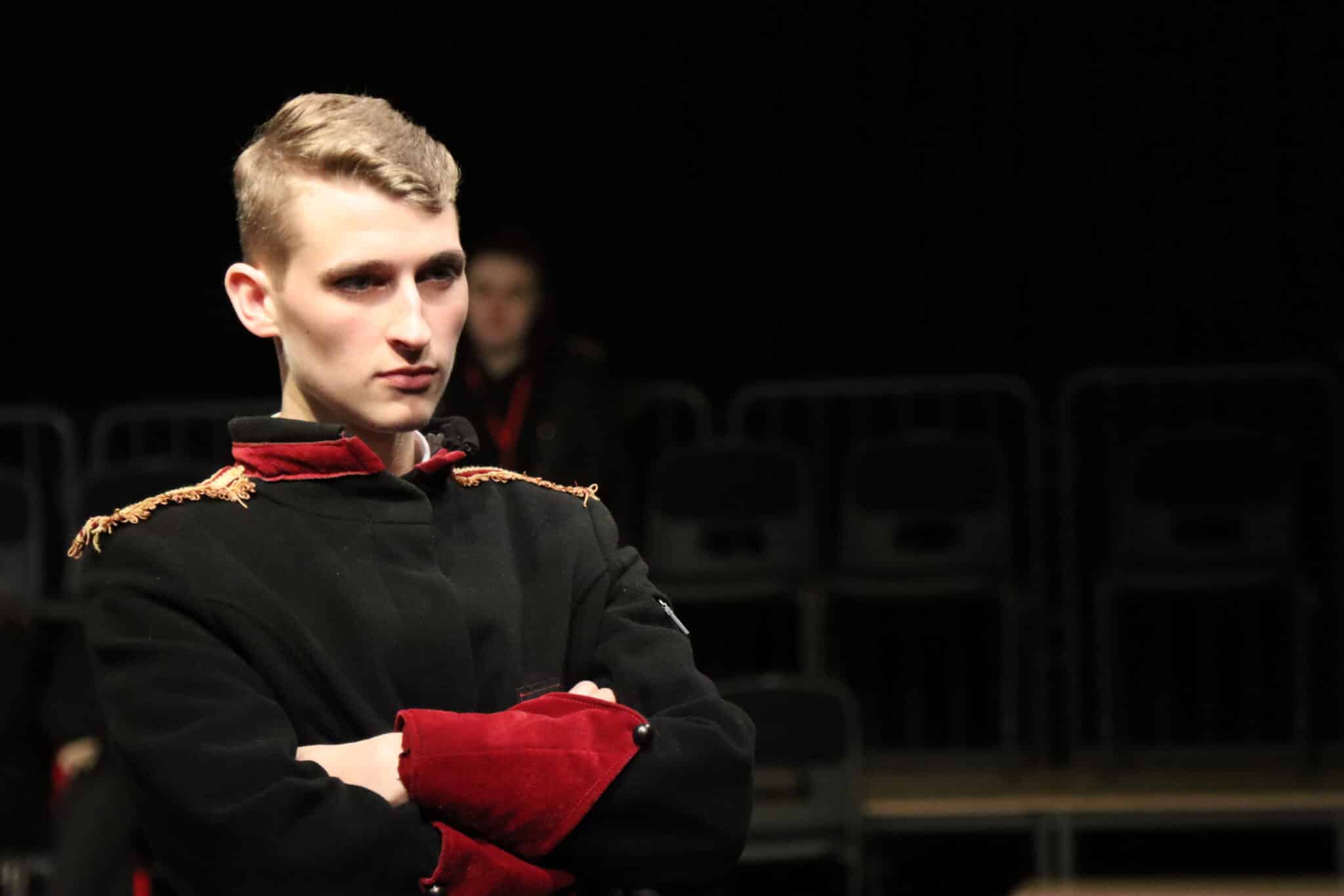 The commander in the play standing with arms crossed