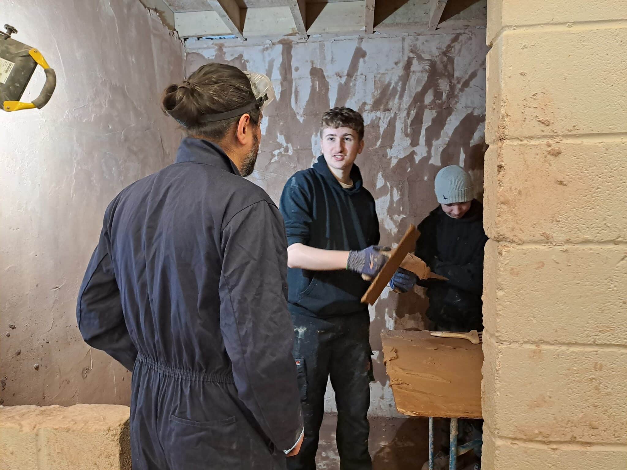 Student teaching his lecturer how to plaster a wall