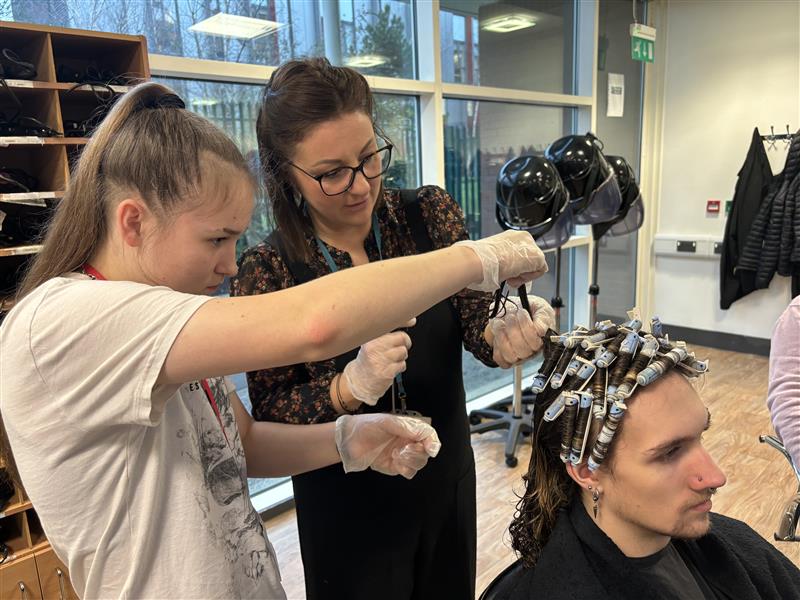 Hairdressing student teaching her lecturer how to do a perm