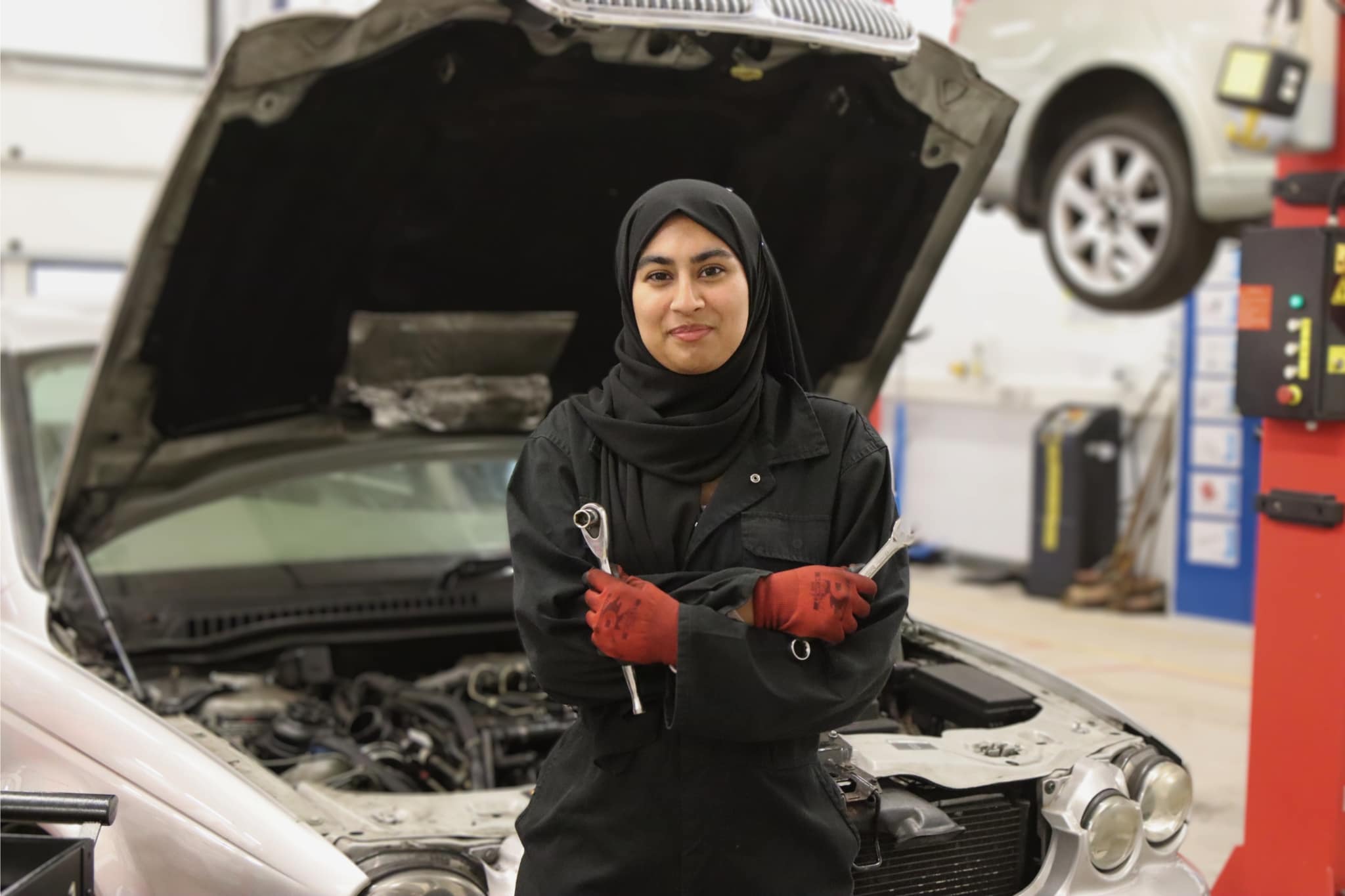 student standing in front a car holding tools and arms crossed