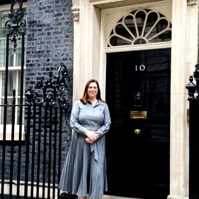 Principal standing in front of the door of 10 downing street wearing a blue dress
