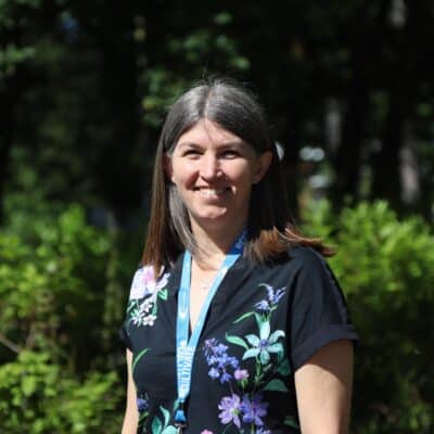 kerry standing and looking at camera in front of greenery