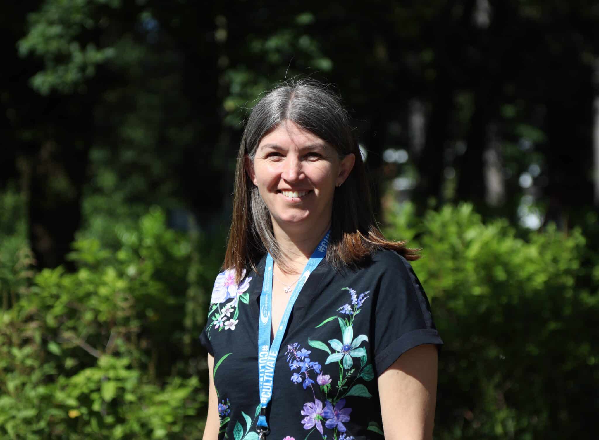 kerry standing and looking at camera in front of greenery