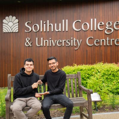 sam and juan sat on bench in front of solihull college & university centre logo