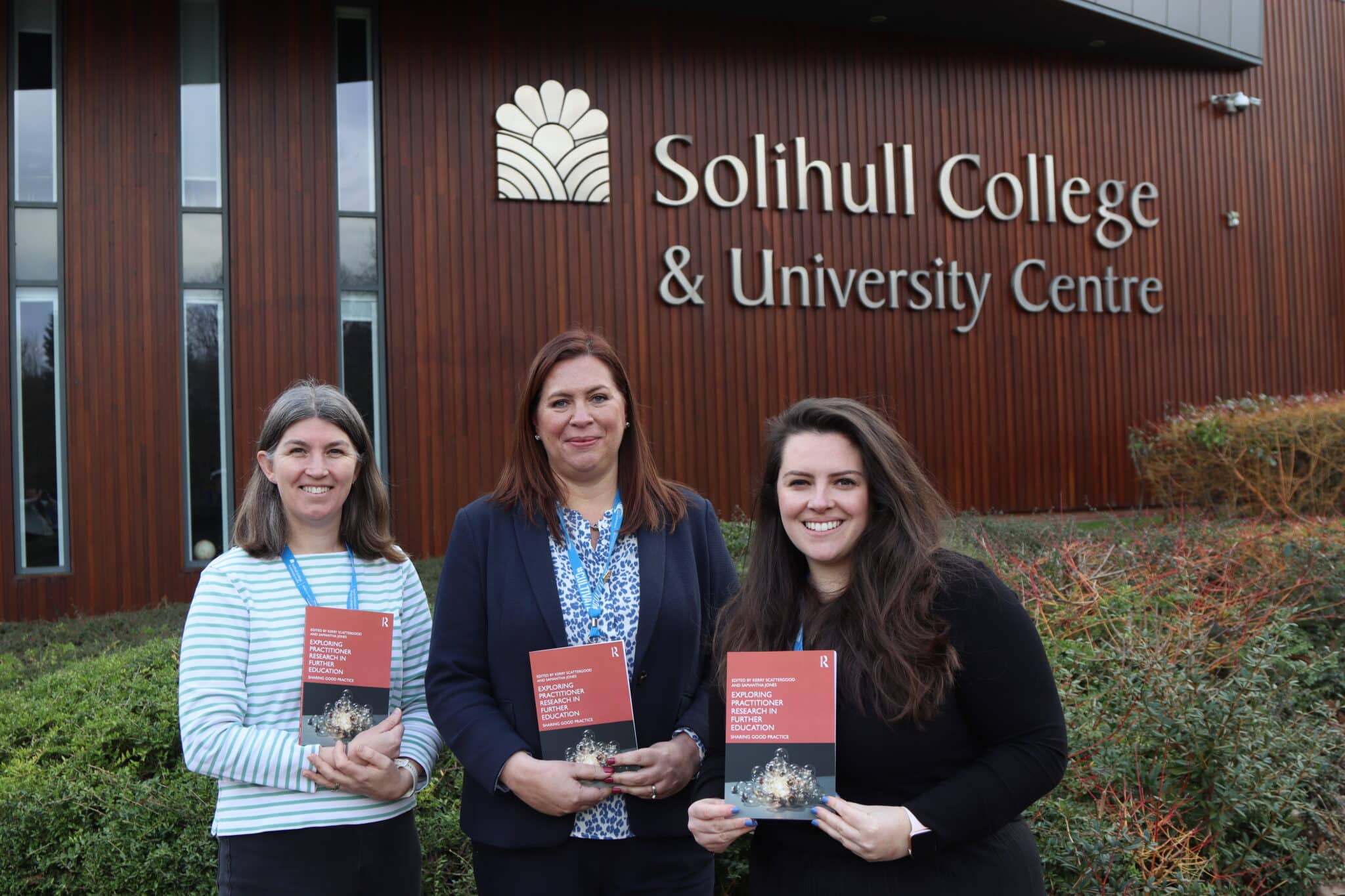3 staff member holding book in front of college
