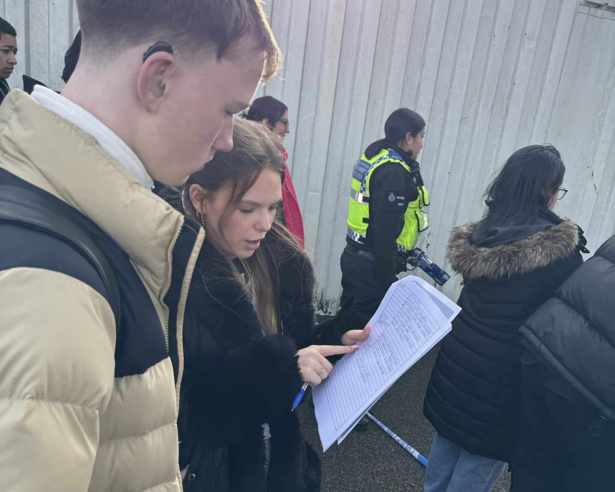 students studying paperwork with police in background